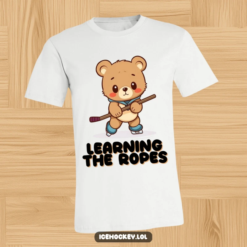 Funny t-shirt featuring a curious bear cub awkwardly attempting to skate while wielding a comically large hockey stick.